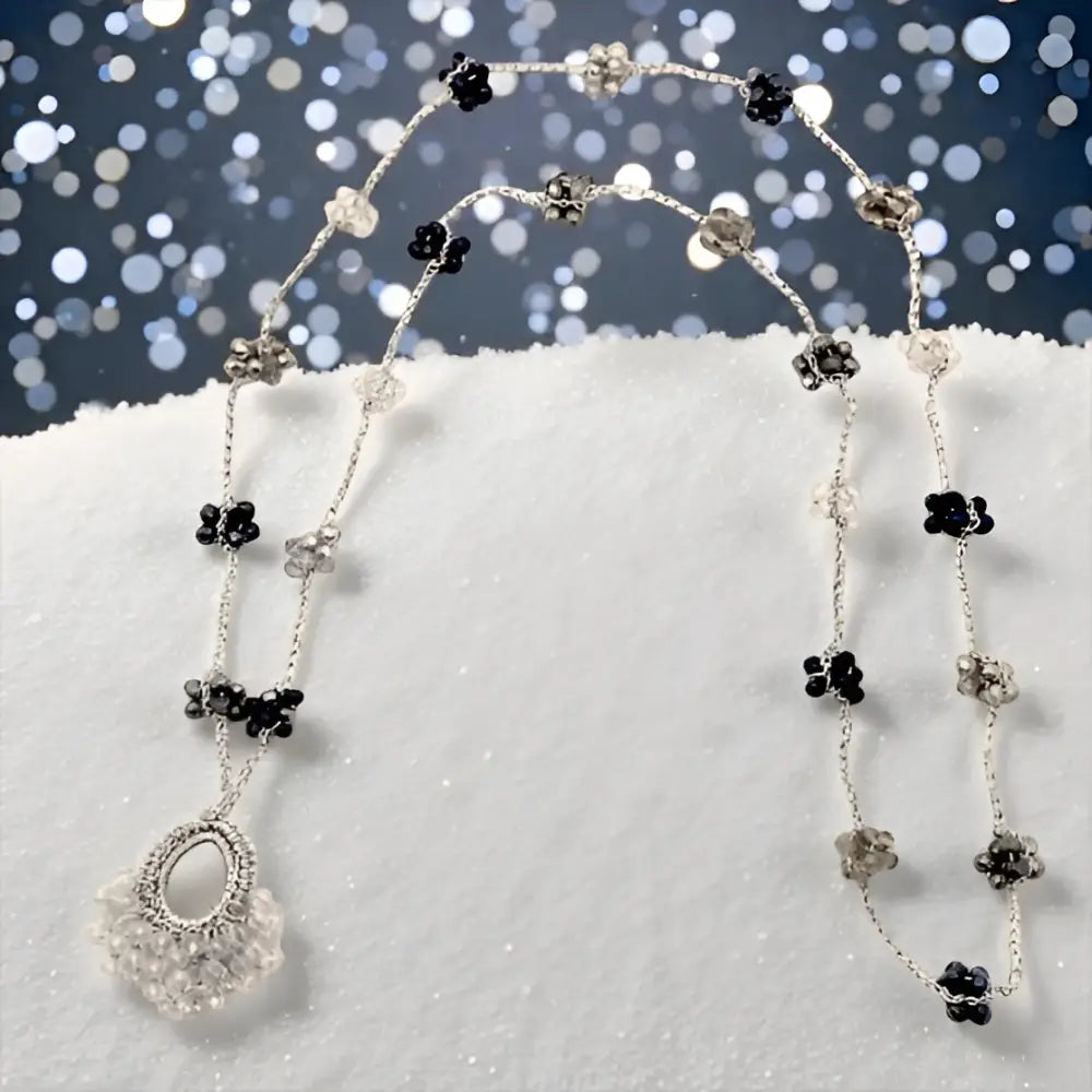 Collana Nebula: intreccio artigianale con perline d’argento, charms floreali neri e chiari, pendente di cristallo